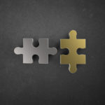 Merging concept illustrated by two different jigsaw piece a silver and a gold one.