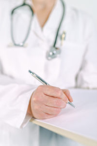 Female doctor in white uniform writing on clipboard 