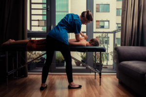A massage therapist treating a female client on a table in an apartment