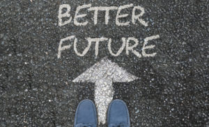 Feet on asphalt road with arrow pointing to better future. 